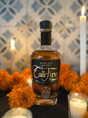 Bottle of Cali Fino tequila surrounded by marigolds and candles on a decorative background