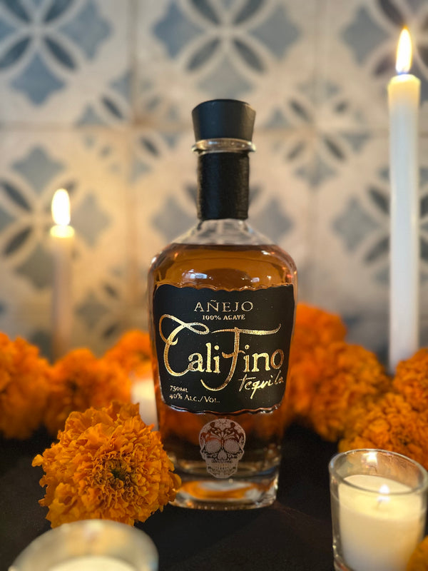 Bottle of Cali Fino tequila surrounded by marigolds and candles on a decorative background